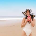 A Woman in a Maillot Drinking a Beverage at the Beach