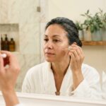 Femme de 45 ans appliquant un sérum visage dans une salle de bain moderne, illustrant les soins de la peau et la fermeté cutanée