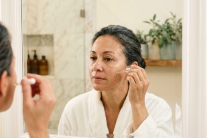 Femme de 45 ans appliquant un sérum visage dans une salle de bain moderne, illustrant les soins de la peau et la fermeté cutanée