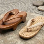 Comparaison entre une paire de geta en bois traditionnels et des zori plats en paille, côte à côte sur une pierre naturelle dans un jardin zen