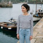 Femme bretonne portant une marinière rayée marine et blanche avec un jean taille haute sur un quai de port en pierre