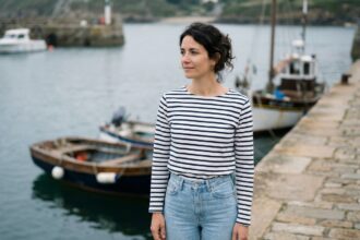 Femme bretonne portant une marinière rayée marine et blanche avec un jean taille haute sur un quai de port en pierre