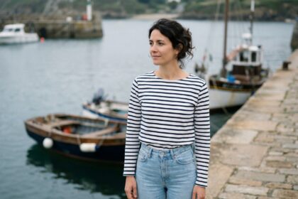 Femme bretonne portant une marinière rayée marine et blanche avec un jean taille haute sur un quai de port en pierre