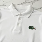 Polo Lacoste blanc avec logo crocodile brodé sur le tissu piqué, vue de dessus sur marbre blanc