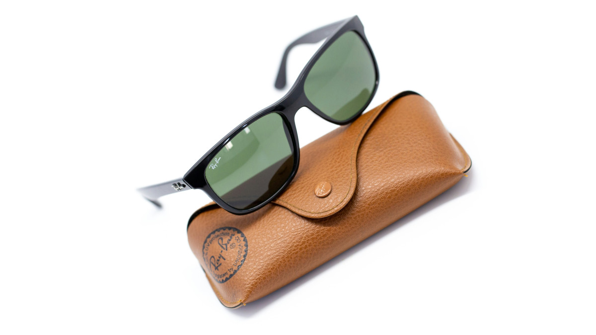 Une paire de rayban posée sur sa pochette sur un fond blanc. 